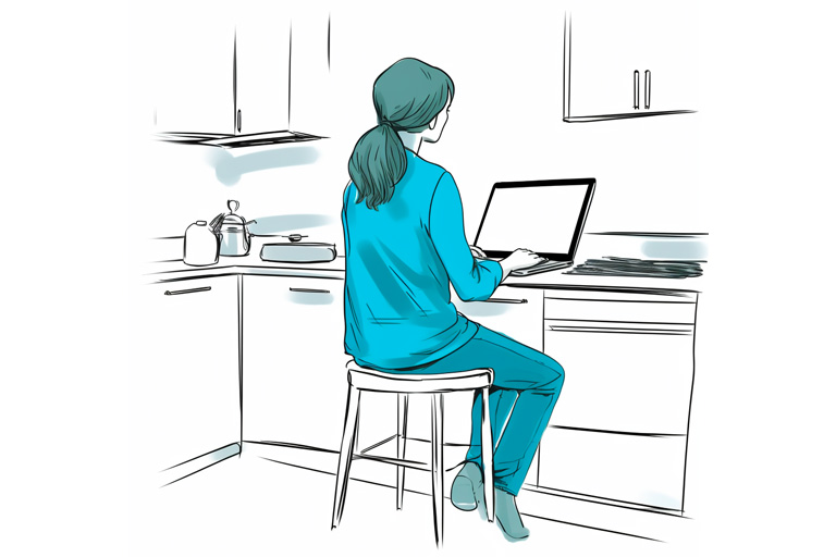 En kvinna sitter vid en dator i ett kök.